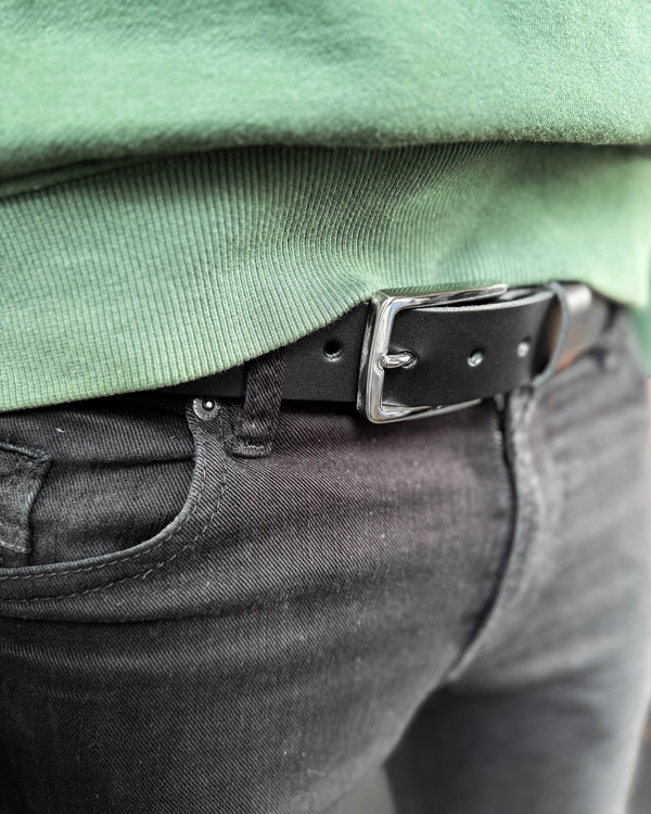 EDGE belt in black leather with silver-coloured steel buckle worn with black jeans and a green sweatshirt