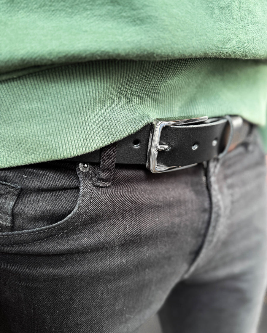 EDGE belt in black leather with silver-coloured steel buckle worn with black jeans and a green sweatshirt