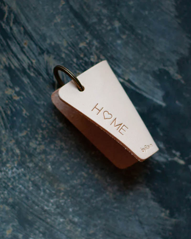 FOLD leather key holder in natural with the engraving "Home" with a heart as the O, lying on a blue patinated surface