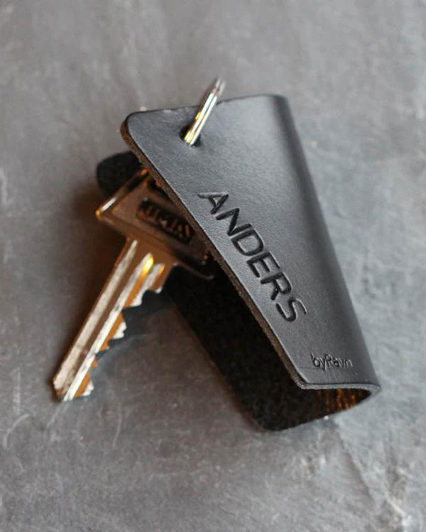 FOLD leather key holder in black with the name "Anders" engraved, with keys on dark slate
