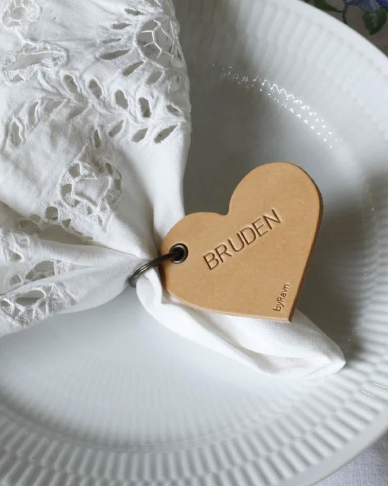 GALLA heart-shaped leather place card in natural with the engraving "Bruden" on a white embroidered napkin and ribbed plate