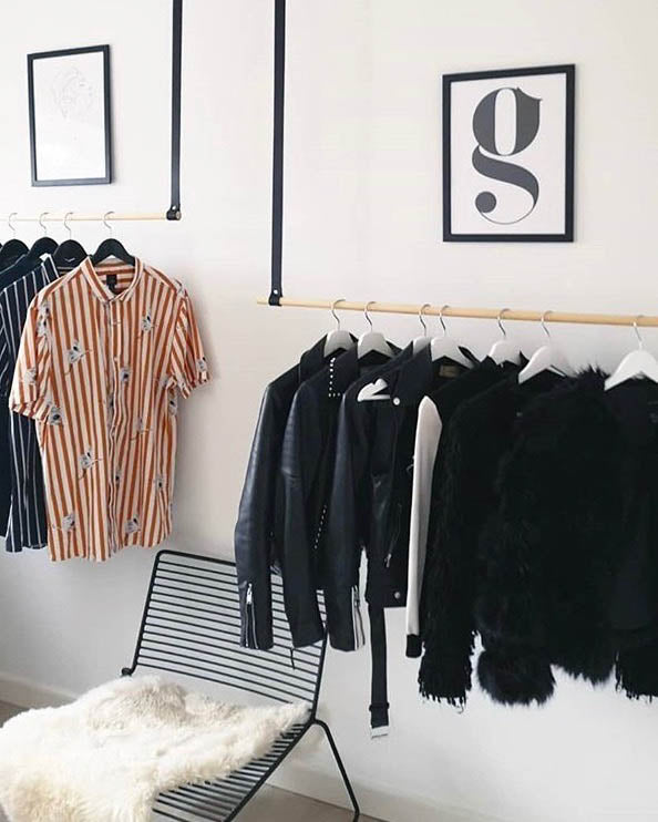 HOLD 15 leather hanging straps in black with clothes on hangers in a bright hallway with chair and poster