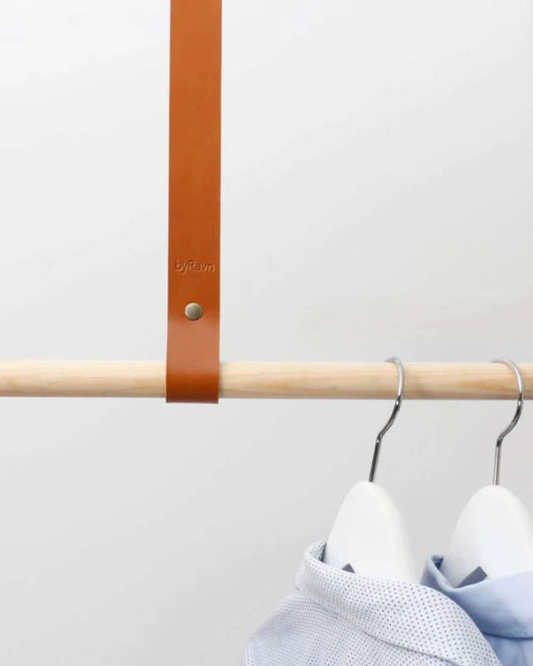 HOLD 15 leather hanging strap in cognac with brass rivet and byRavn embossing around a wooden rail with shirts on hangers