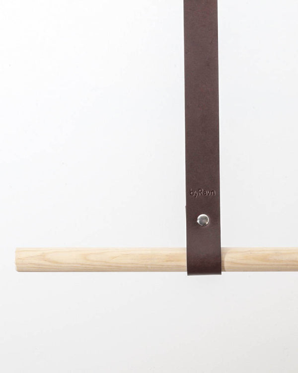 HOLD 15 leather hanging strap in dark brown with silver-coloured rivet and byRavn embossing around a light wooden rail