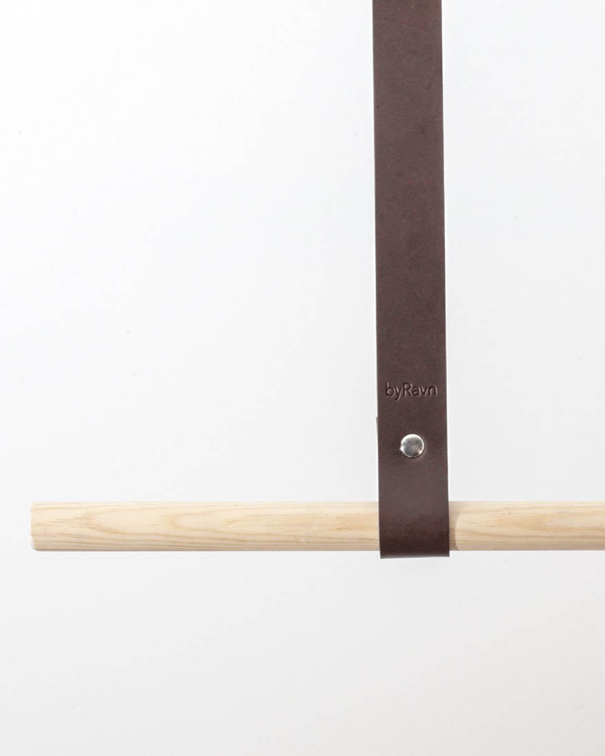 HOLD 15 leather hanging strap in dark brown with silver-coloured rivet and byRavn embossing around a light wooden rail