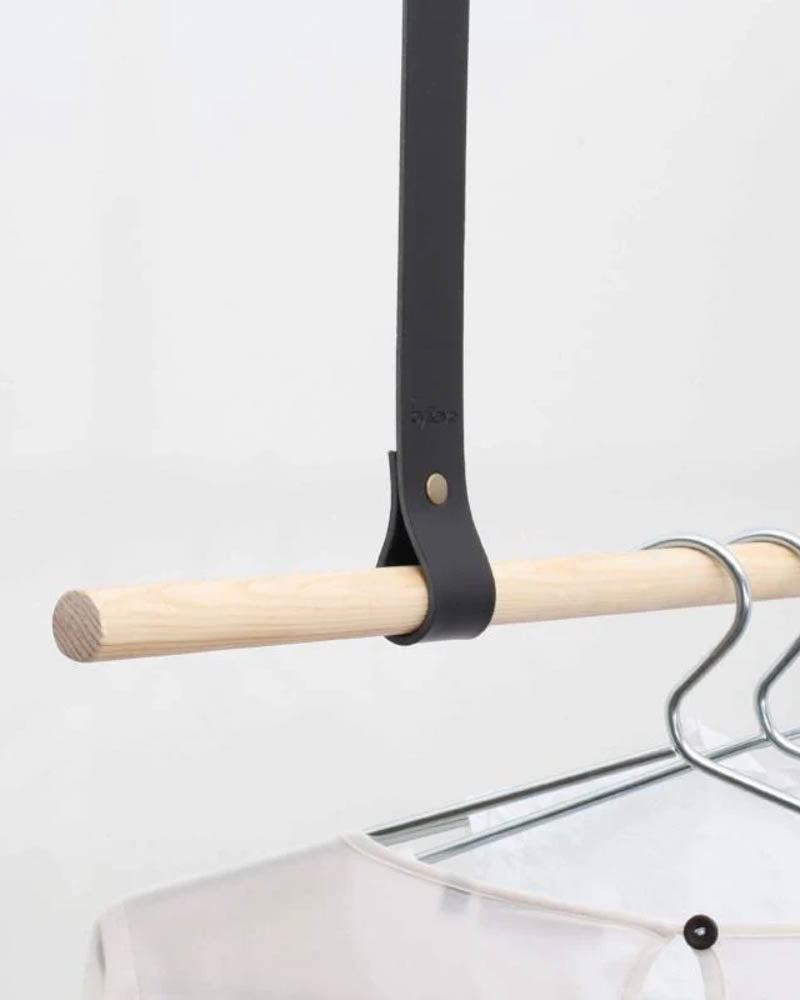 HOLD 15 leather hanging strap in black with rivet around a light wooden rail with hangers and a white blouse