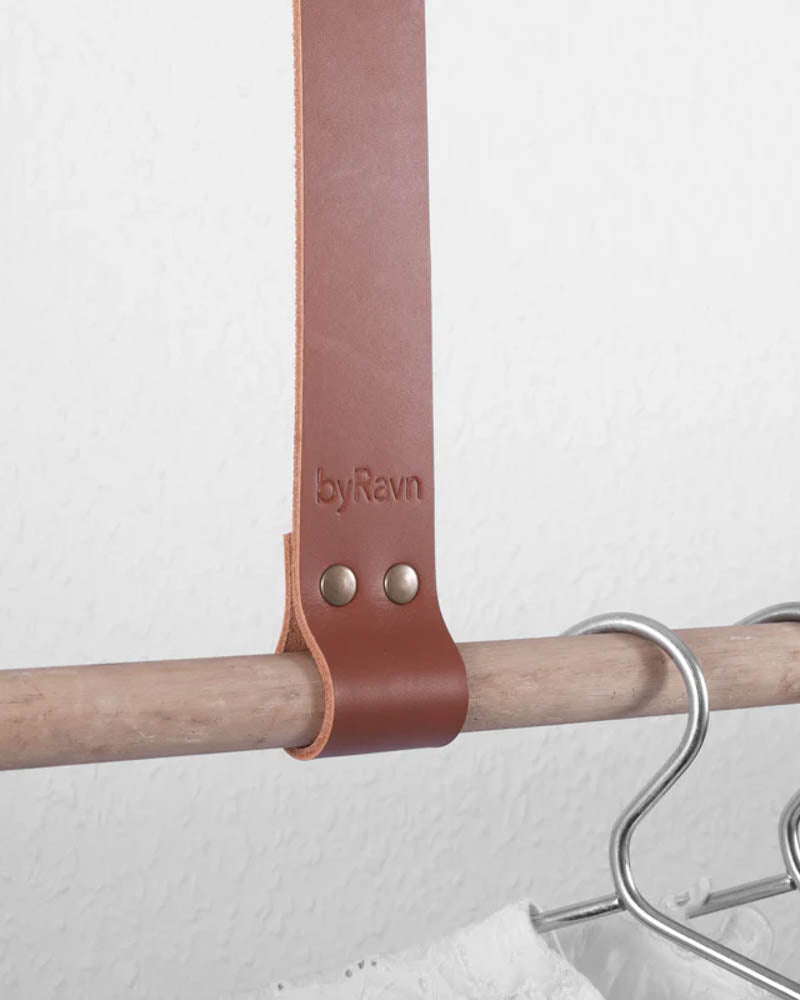 HOLD 30 hanging strap in cognac full-grain leather with two brass rivets and byRavn embossing around a wooden rail with hangers
