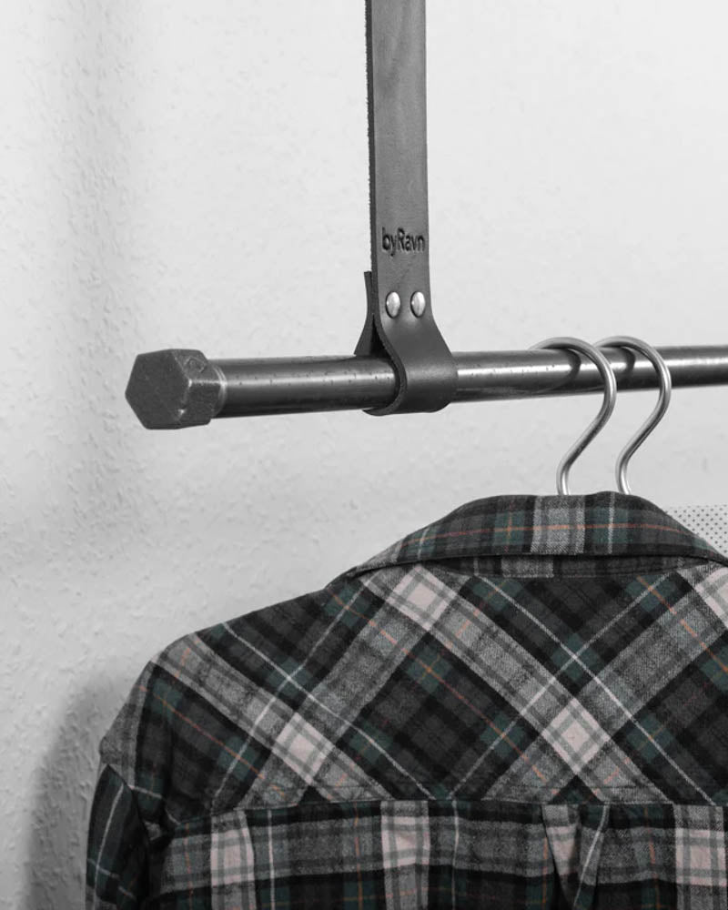 HOLD 30 hanging strap in black leather with two rivets and byRavn embossing around a metal rail with a checked shirt on a hanger
