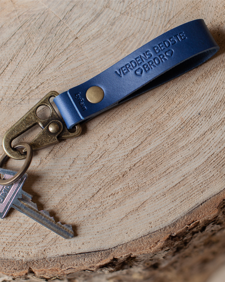 HOOK leather keyring in navy blue with the engraving "Verdens bedste bror" and hearts, with key on a wooden slice