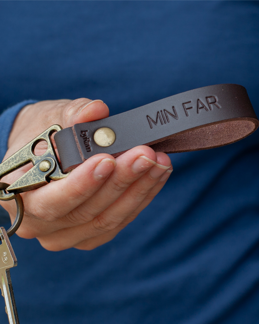 HOOK leather keyring in dark brown with antique brass carabiner and the engraving "Min far", held in hand with key
