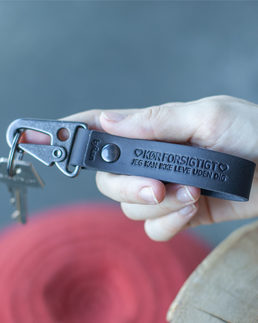 HOOK leather keyring in black with black carabiner and the engraving "Kør forsigtigt – jeg kan ikke leve uden dig" ♡ held in hand
