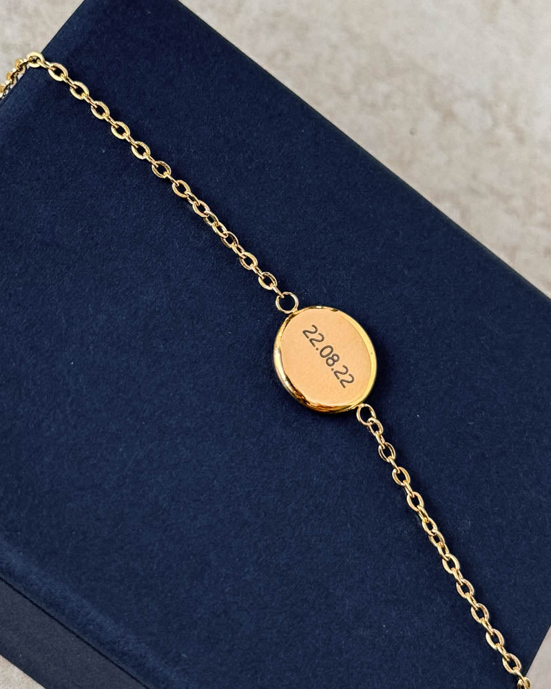 IBI NOTE bracelet in gold-plated stainless steel with the date "22.08.22" engraved on a round disc, lying on a navy blue jewellery box