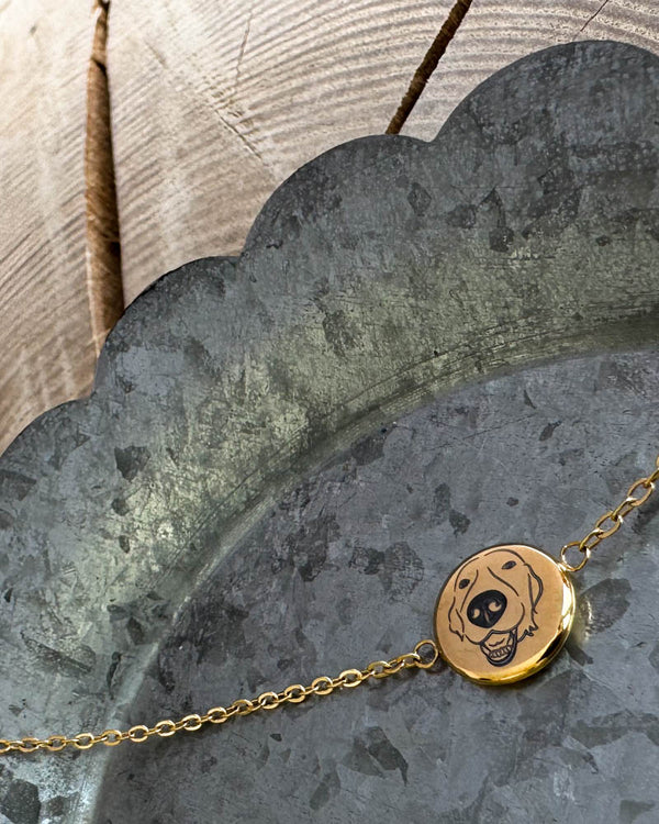 IBI PORTRAIT bracelet in gold-plated stainless steel with a drawing of a dog engraved on a round disc, lying on a zinc tray