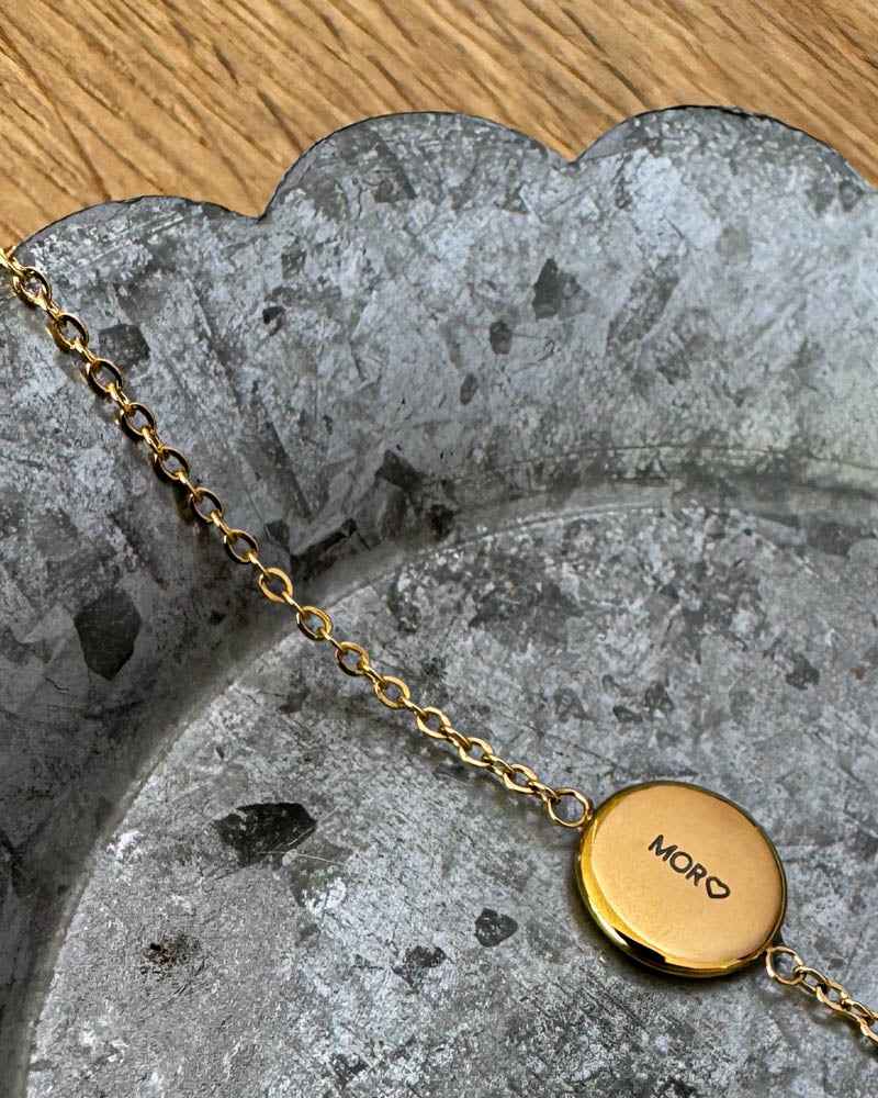 IBI QUOTE bracelet in gold-plated stainless steel with the engraving "Mor" ♡ on a round disc, lying on a zinc tray