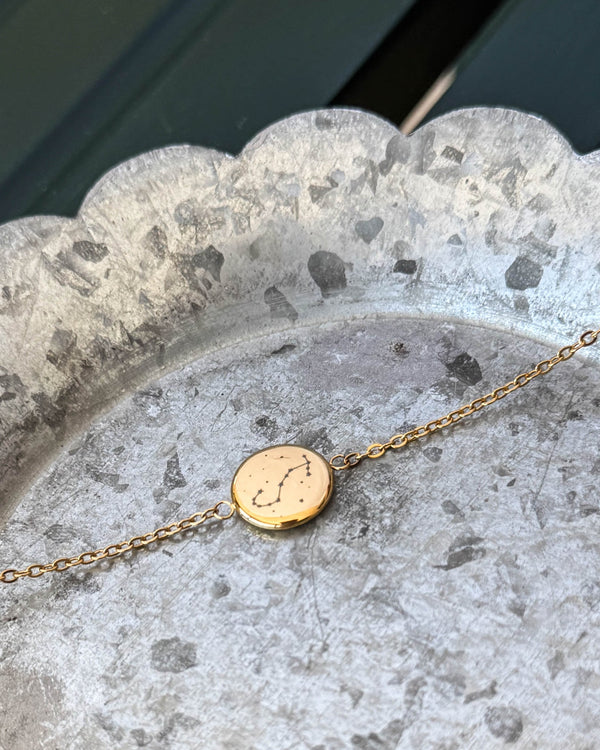 IBI STAR bracelet in gold-plated stainless steel with the Scorpio constellation engraved on a round disc, lying on a zinc tray