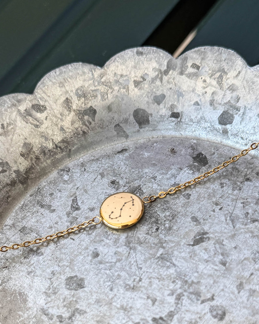 IBI STAR bracelet in gold-plated stainless steel with the Scorpio constellation engraved on a round disc, lying on a zinc tray