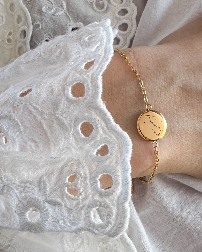 IBI STAR bracelet in gold-plated stainless steel with constellation engraved on a round disc, worn on the wrist with a white lace blouse