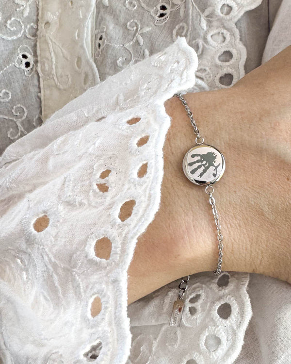 IBI MOTIF bracelet in silver-coloured stainless steel with engraved handprint, worn on the wrist with a white lace blouse