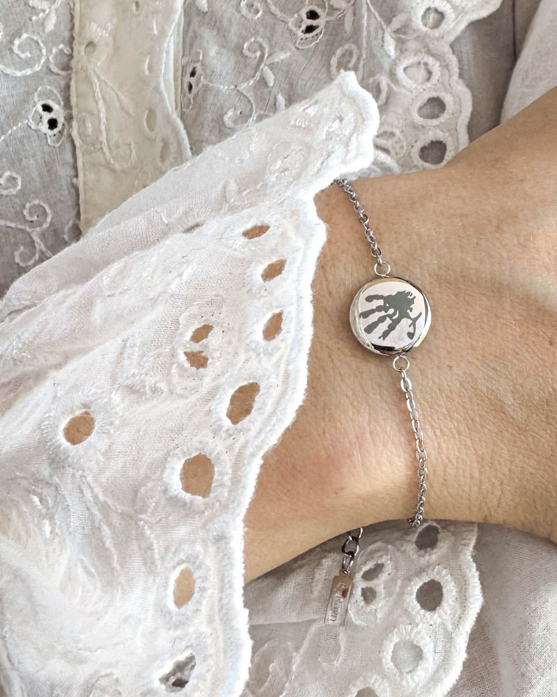 IBI MOTIF bracelet in silver-coloured stainless steel with engraved handprint, worn on the wrist with a white lace blouse