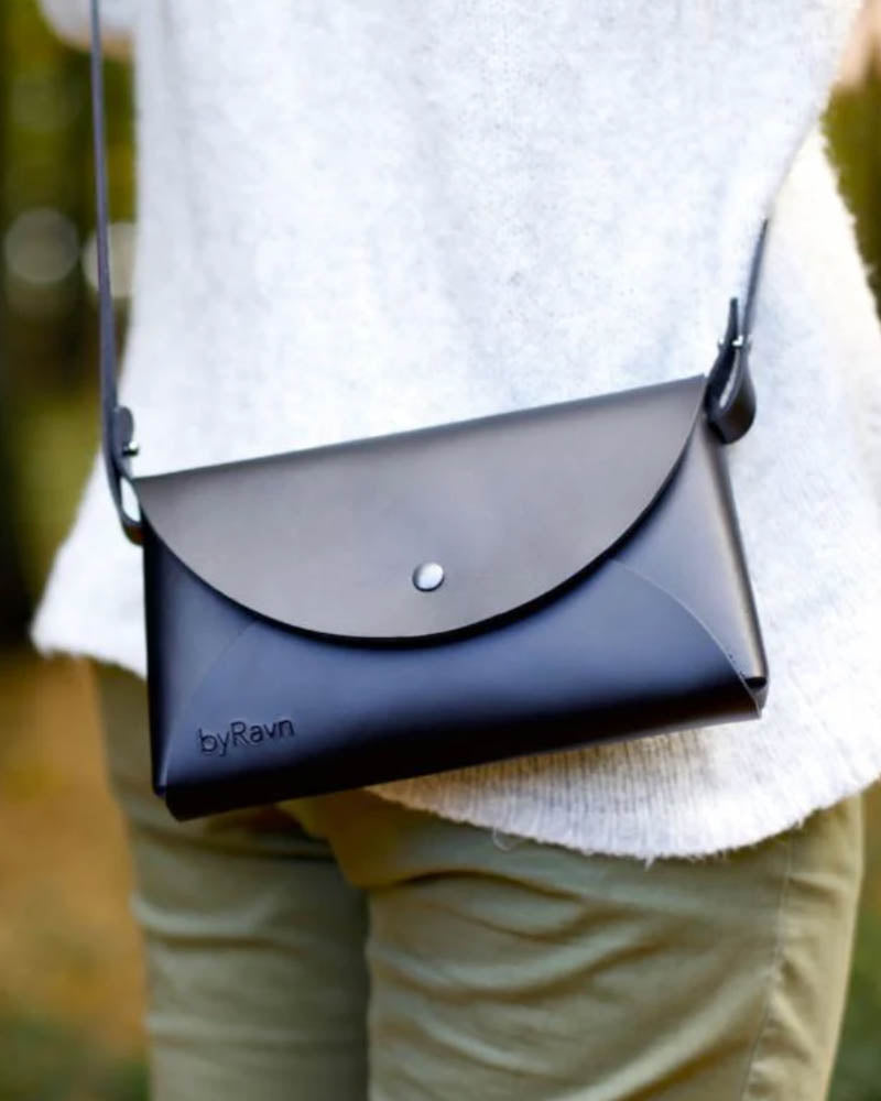 INA shoulder bag in black leather worn over the shoulder with a white knit jumper and light green trousers