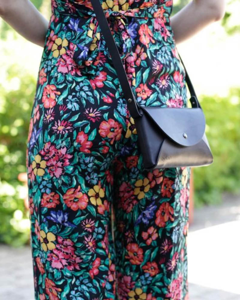 INA shoulder bag in black leather worn crossbody with a floral jumpsuit in the garden
