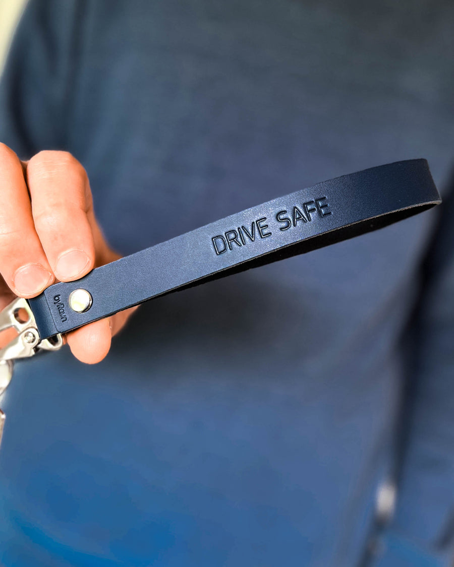 IRON leather keyring in navy blue with long strap and the engraving "Drive safe", held in hand