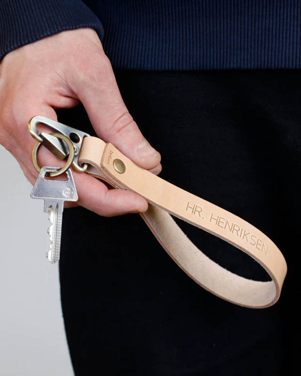 IRON leather keyring in natural with long wrist strap and the engraving "Hr. Henriksen", held in hand with key