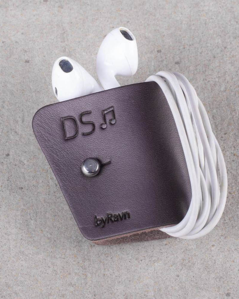KAX earbud clip in dark brown leather with white earpods wrapped around and the engraving "DS" with a music note, on concrete