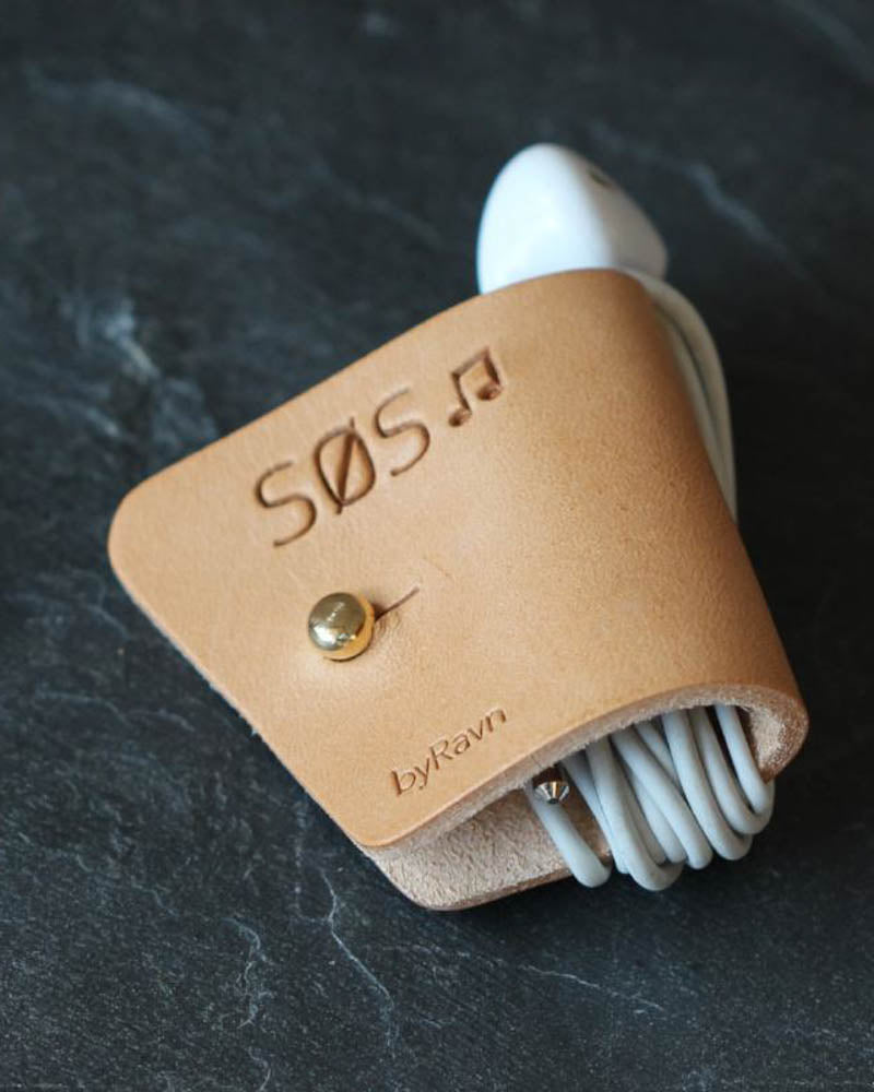 KAX leather earbud holder in natural with the engraving "Søs" ♪ and brass stud, with earpods on dark slate