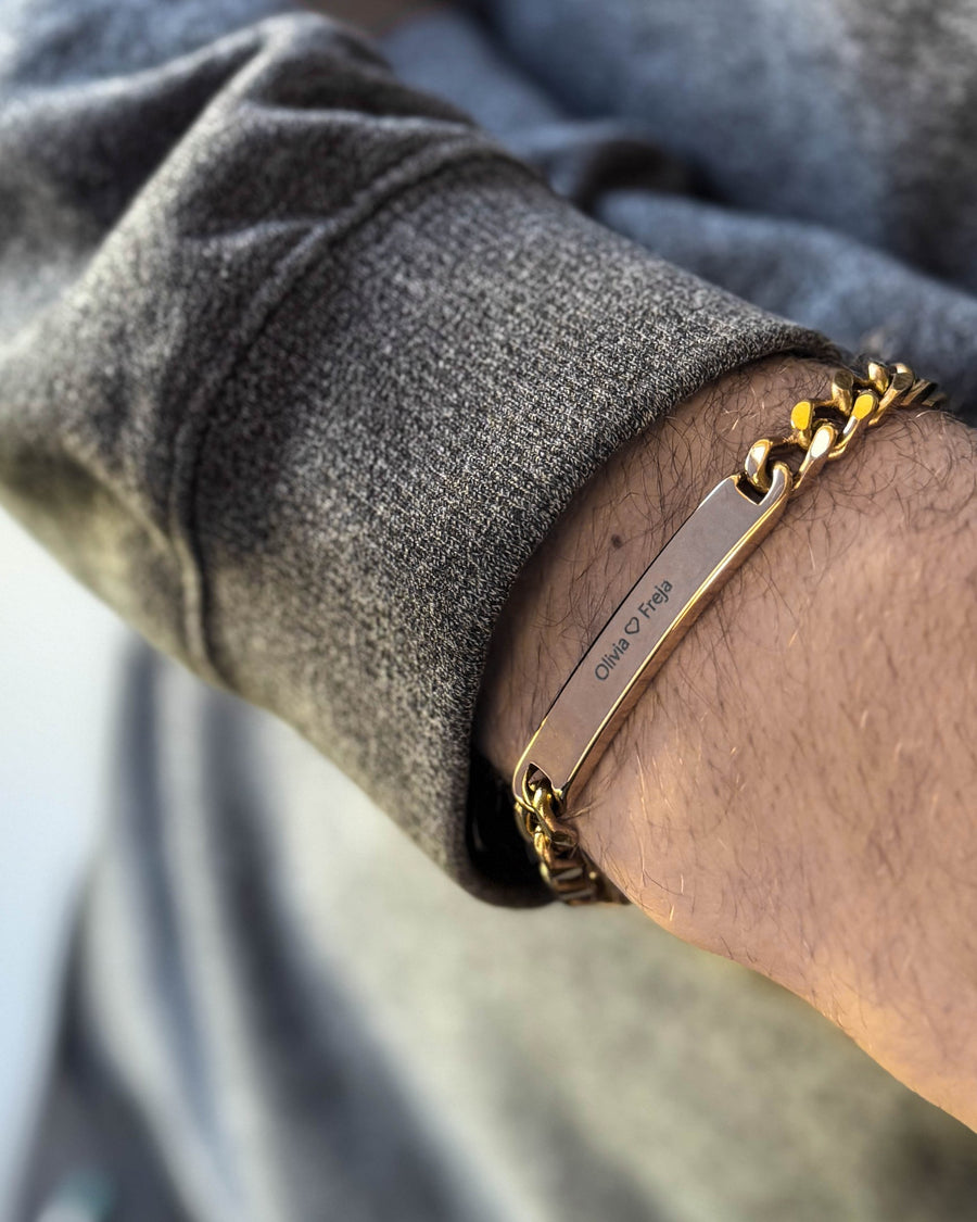 LEO name bracelet in gold-plated stainless steel with the engraving "Olivia ♡ Freja" on a man's wrist, grey sweatshirt