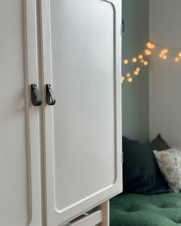 LOOP leather handles in dark brown on a cream wardrobe beside a bed with green duvet and fairy lights