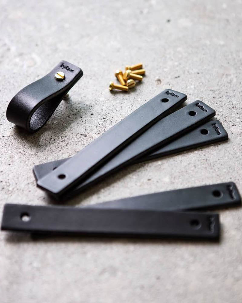 LOOP leather drawer pulls in black, several leather strips with byRavn embossing, one assembled pull and brass screws on concrete