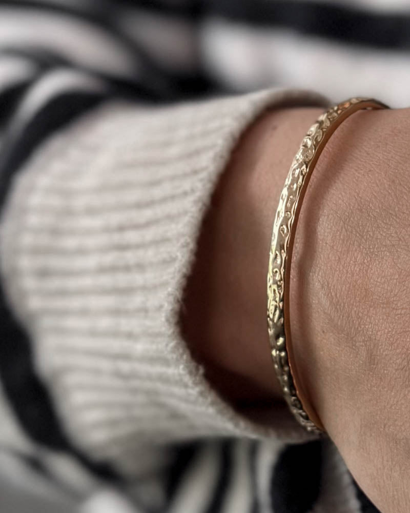 LUNA bracelet in gold-plated stainless steel with hammered finish on the wrist, white knit and striped blouse
