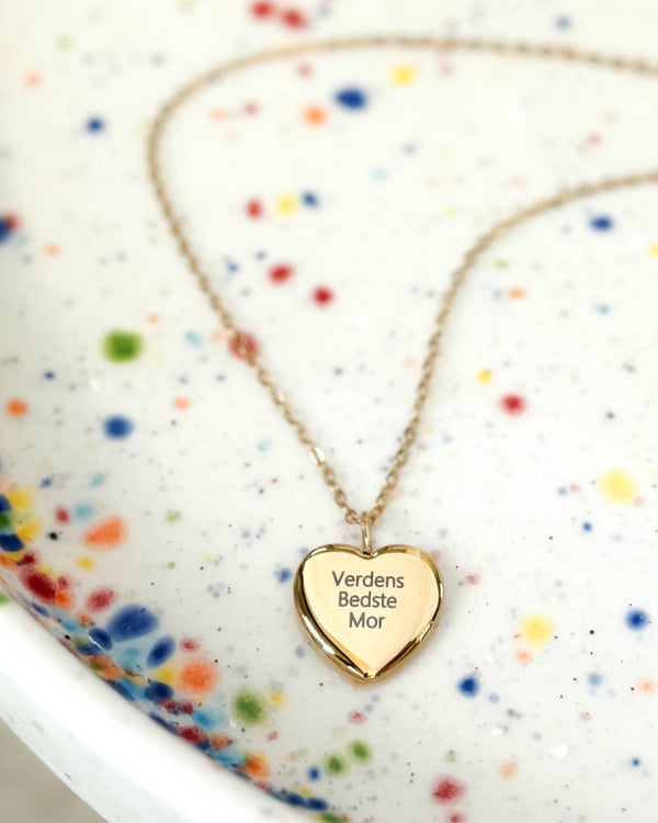 LUV QUOTE necklace in gold-plated stainless steel with the engraving "Verdens Bedste Mor" on a heart pendant, on a speckled ceramic dish
