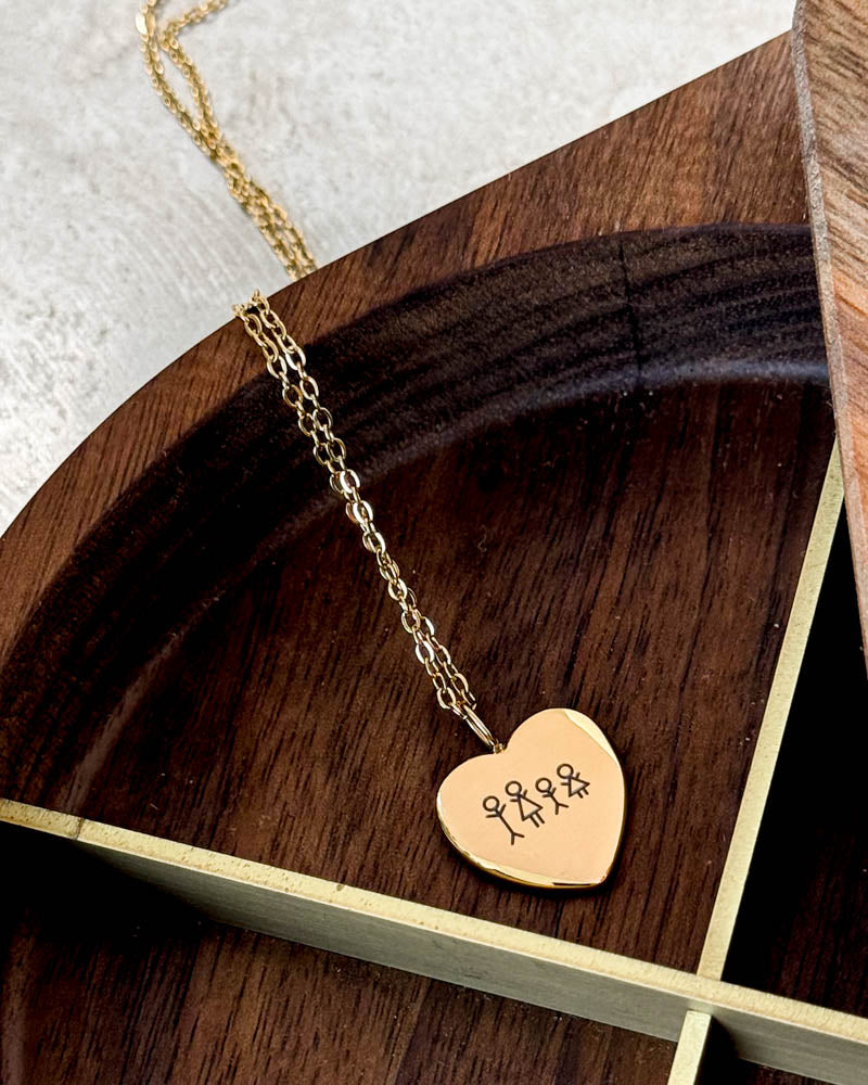 LUV STICK necklace in gold-plated stainless steel with matchstick family engraved in heart, on a round wooden tray with brass edges