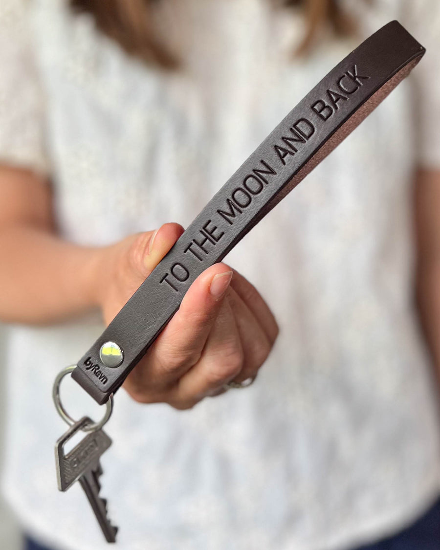 LUX leather keyring in dark brown with personalised engraving "To the moon and back", held in hand with keys