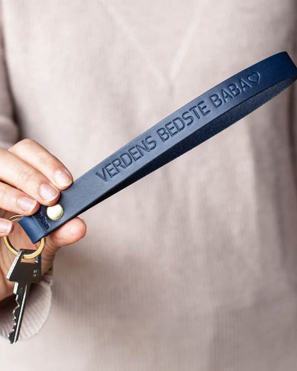 LUX leather keyring in navy blue with brass rivet and the engraving "Verdens bedste baba" ♡, held in hand with key