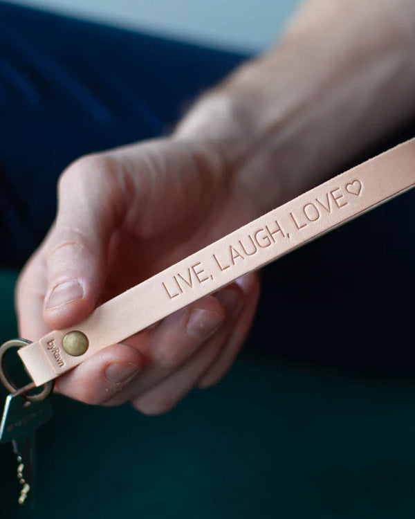 LUX leather keyring in natural with brass rivet and personalised engraving "Live, laugh, love" ♡, held in hand with key