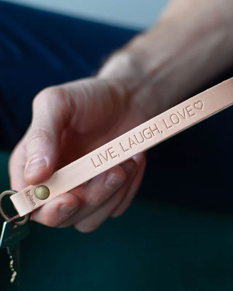 LUX leather keyring in natural with brass rivet and personalised engraving "Live, laugh, love" ♡, held in hand with key