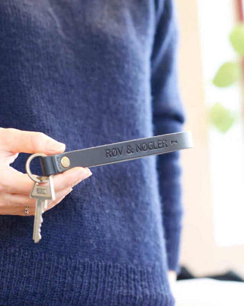 LUX leather keyring in black with the engraving "Røv & nøgler" and a small key symbol, held in hand with key