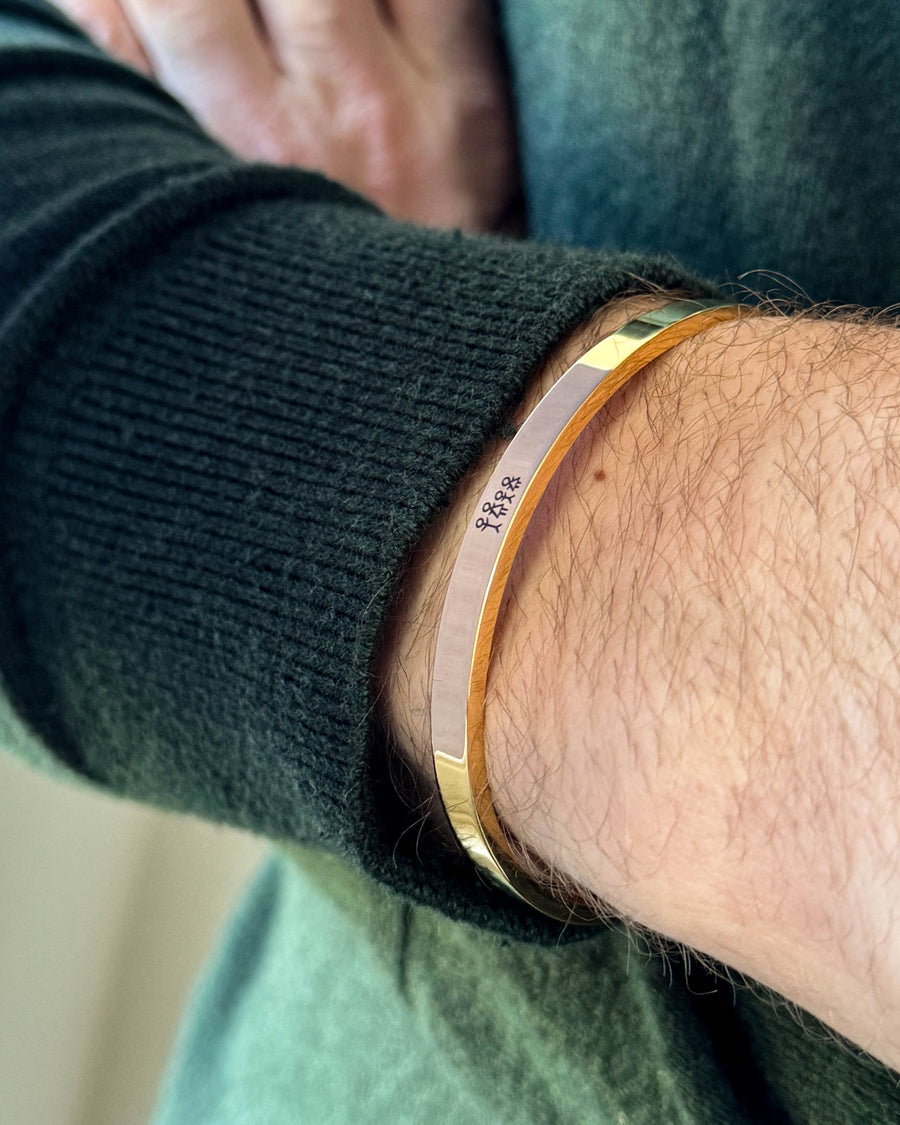 MARS STICK bracelet in gold-plated stainless steel with engraved matchstick family, worn on the wrist with a dark green knit