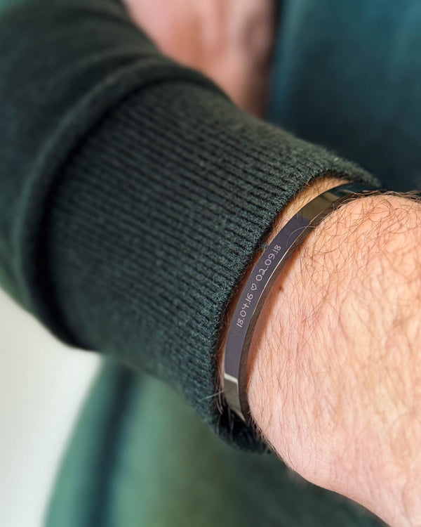 MARS SCRIPT bracelet in black stainless steel with the dates "18.04.16 ♡ 02.09.18" engraved in handwriting, worn with a dark green knit