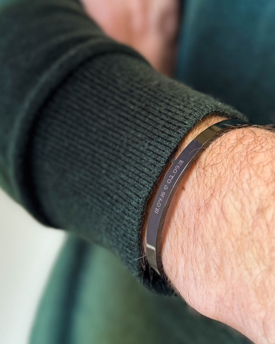 MARS SCRIPT bracelet in black stainless steel with the dates "18.04.16 ♡ 02.09.18" engraved in handwriting, worn with a dark green knit