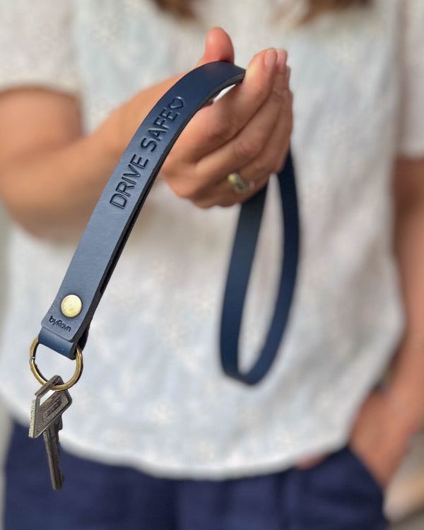 MAX leather keyring in navy blue as a long strap with brass rivet and the engraving "Drive safe" ♡, held in hand with key