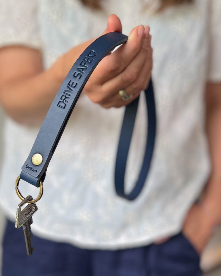 MAX leather keyring in navy blue as a long strap with brass rivet and the engraving "Drive safe" ♡, held in hand with key