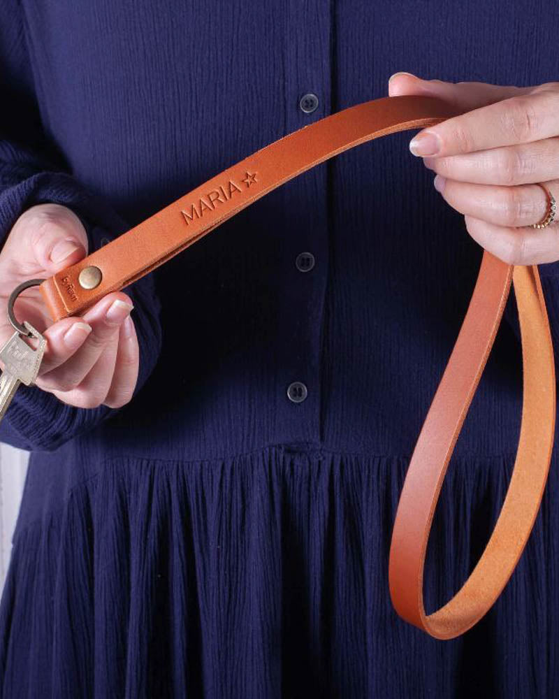 MAX leather keyring in cognac, long strap with the name "Maria" ☆ engraved, held in both hands with keys against a navy blue dress