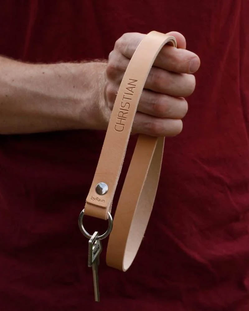 MAX leather keyring in natural as a long strap with the name "Christian" engraved, held in hand with key