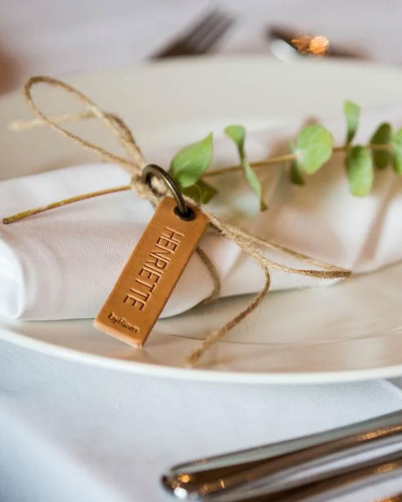 Sample of the MERRY leather place card in natural with the name "Henriette" engraved, tied around a napkin with eucalyptus