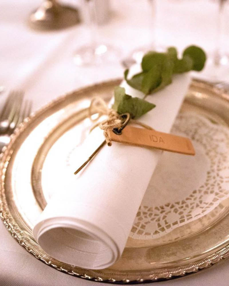 MERRY leather place card in natural with the name "Ida" engraved around a rolled napkin on a gold plate with lace paper