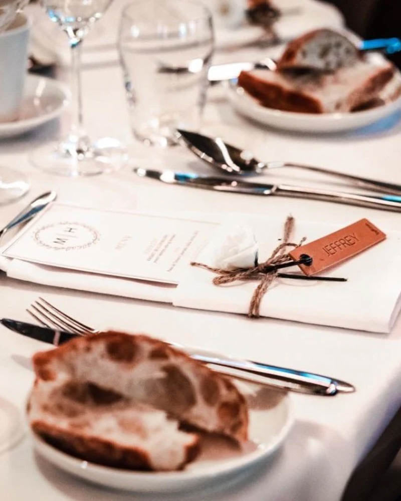 Sample of the MERRY leather place card in cognac with the name "Jeffrey" engraved beside menu card and bread on the party table